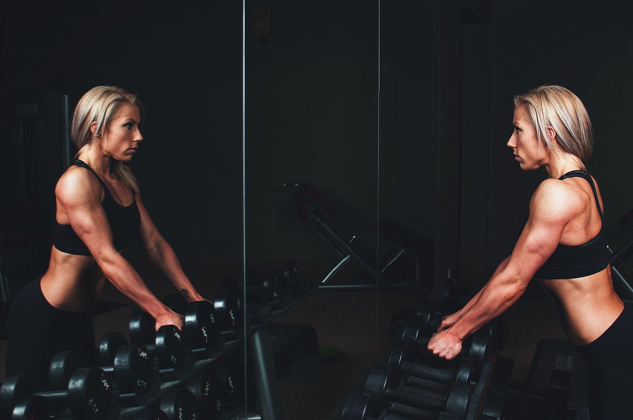 kobieta podnosząca hantle widzi siebie w lustrze